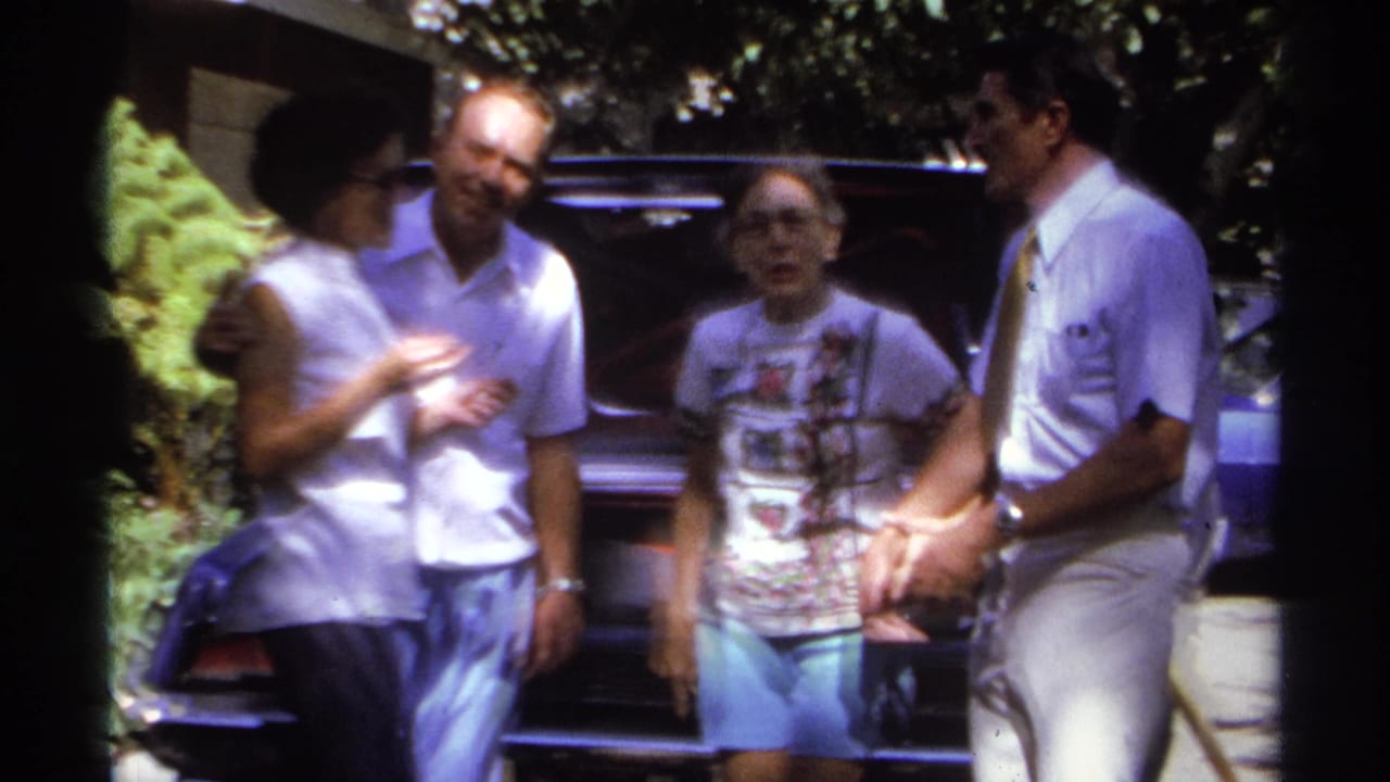Four adults in casual 1970s clothing gather beside a dark car outdoors in La Paz, Mexico, according to clip metadata.