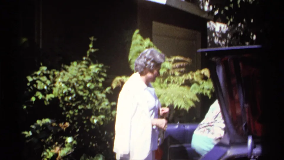 1974 La Paz home-movie frame showing adults gathered near greenery and a shaded porch area.