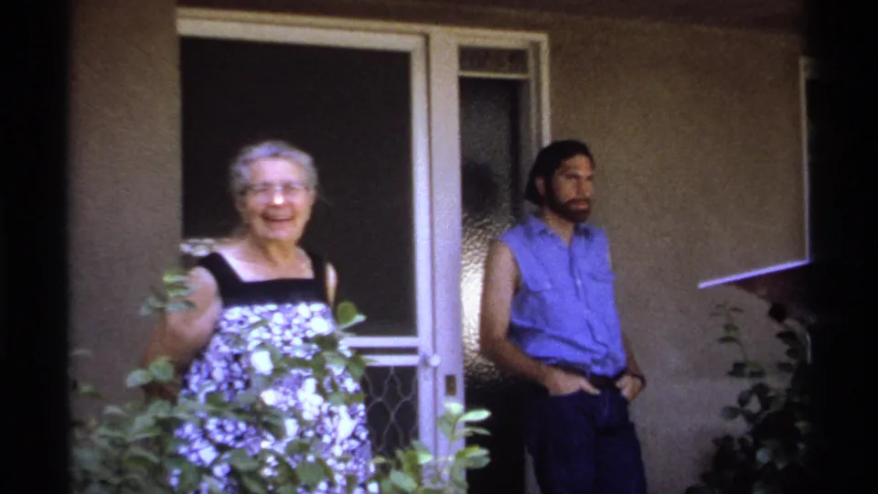 In La Paz, Mexico, an elderly woman smiles on a porch near a man in a blue sleeveless shirt.