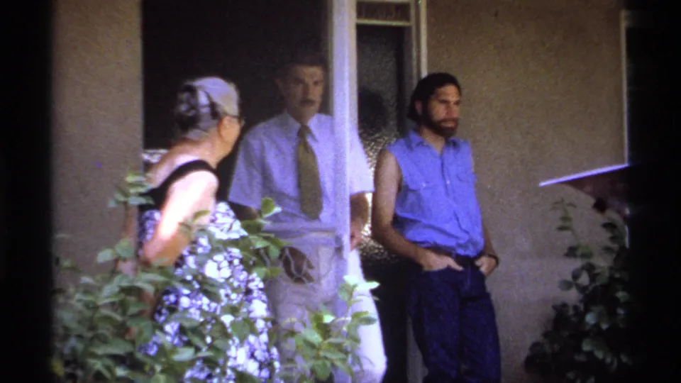 La Paz home-movie frame showing a woman, a man in a white shirt and tie, and another man on a porch.