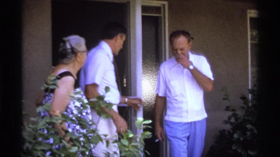 The older woman and two men gather outside the house doorway in La Paz, Mexico, with foliage framing the 1974 home-movie shot.