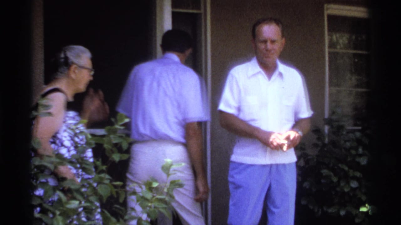 In La Paz, Mexico in 1974, adults gather near a shaded doorway while a man in a white shirt faces the 8mm camera.