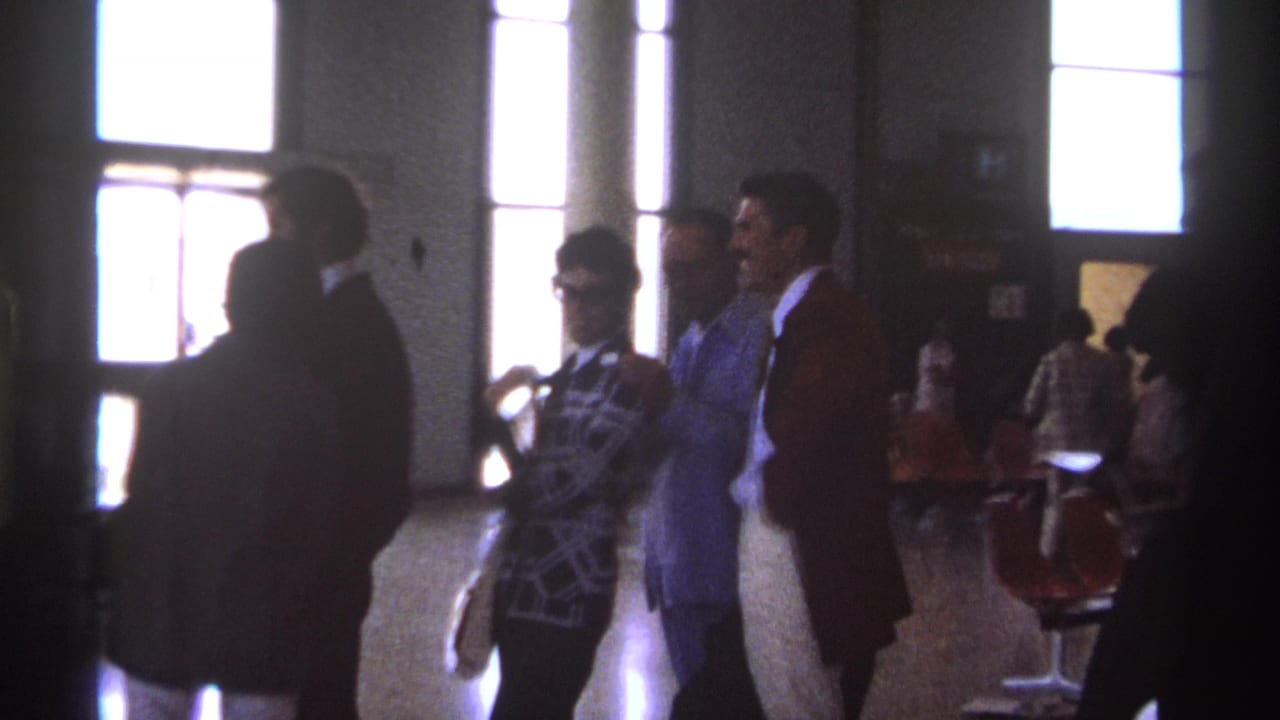 Passengers wait inside an airport area near tall bright windows.