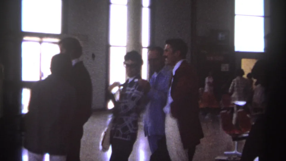 1974 La Paz airport home-movie frame showing people waiting indoors, silhouetted by bright windows near the boarding area.