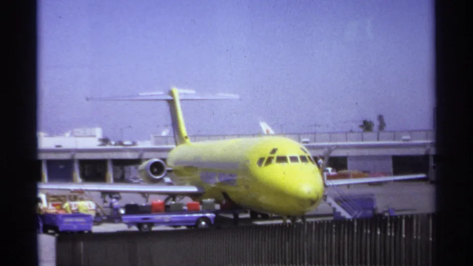 Yellow aircraft parked at the La Paz airport in 1974 while baggage carts and ground activity appear near the nose and wing.