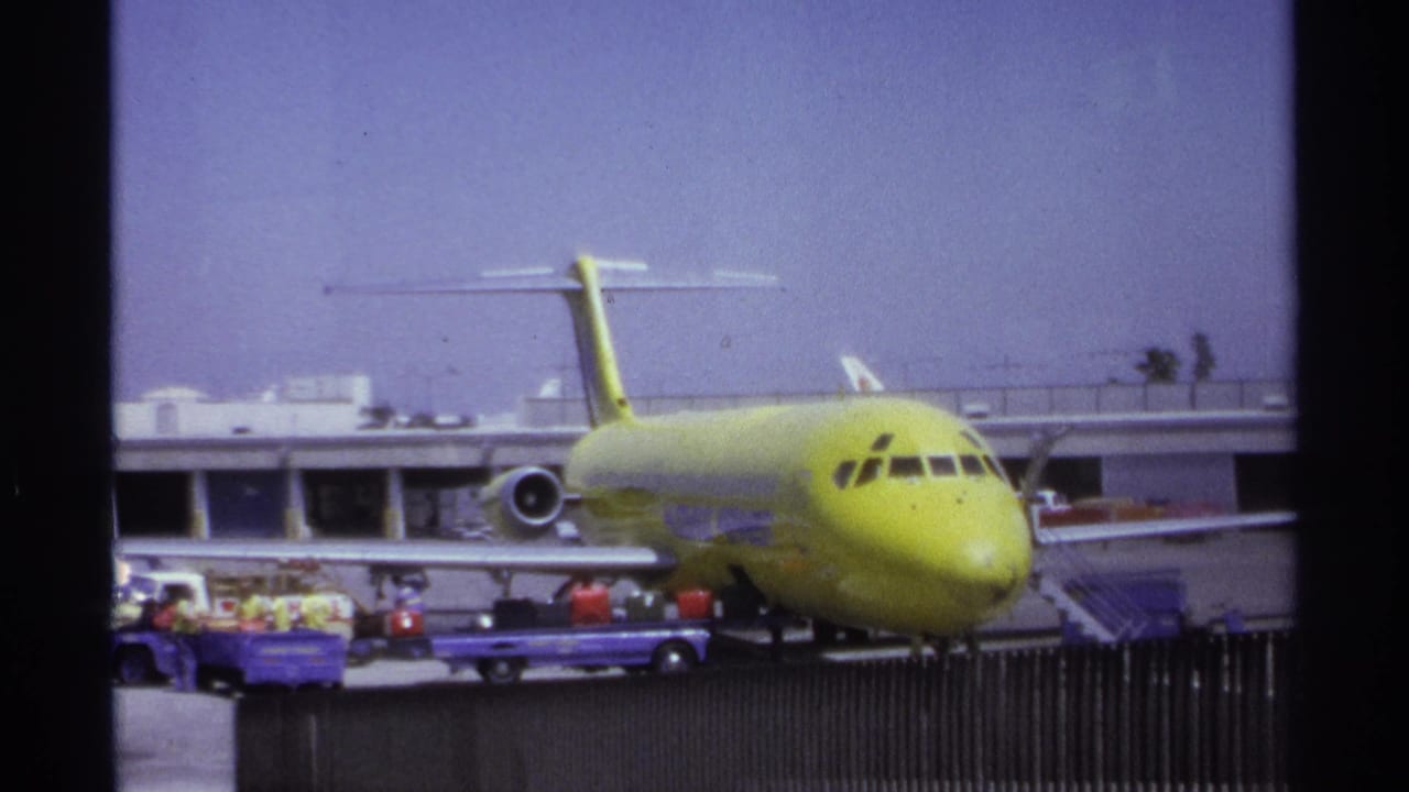 Lime-green airplane at an airport gate while ground crew handle luggage near baggage carts.