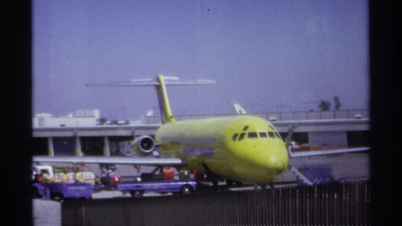 Parked lime-green airplane with baggage carts and workers visible near the terminal.
