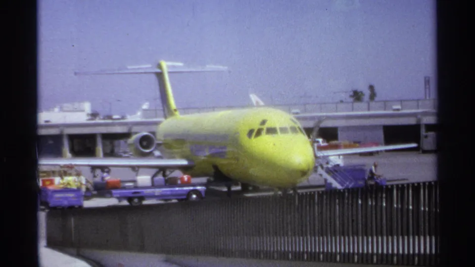 Home-movie frame of a yellow commercial aircraft at La Paz airport, with cargo carts and crew visible near the terminal.