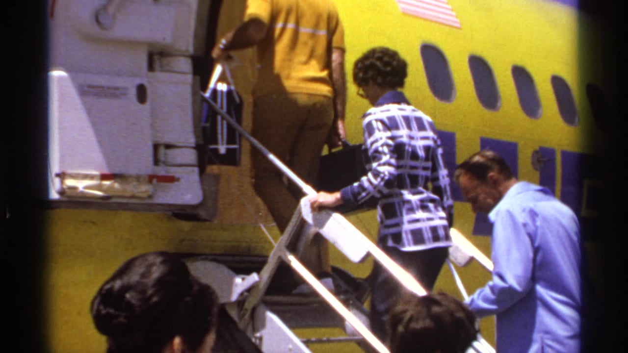 A woman in a patterned jacket walks up aircraft stairs beside a yellow airplane.