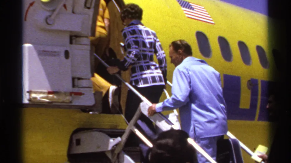 Travelers climb into a yellow commercial airplane in La Paz, Mexico, with a man in blue following and the fuselage flag visible.