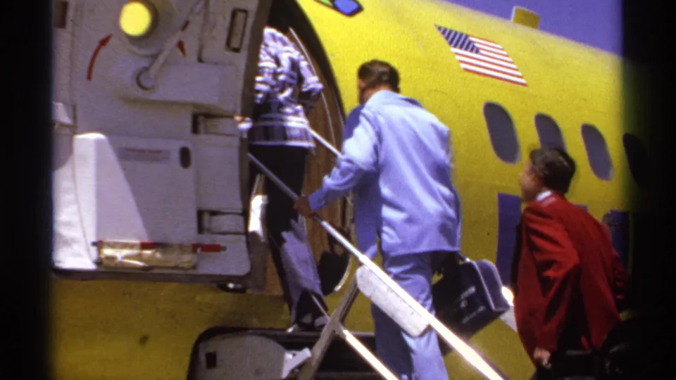 At the end of the clip, a man in a light blue shirt carries luggage up the mobile stairs toward the yellow aircraft doorway.