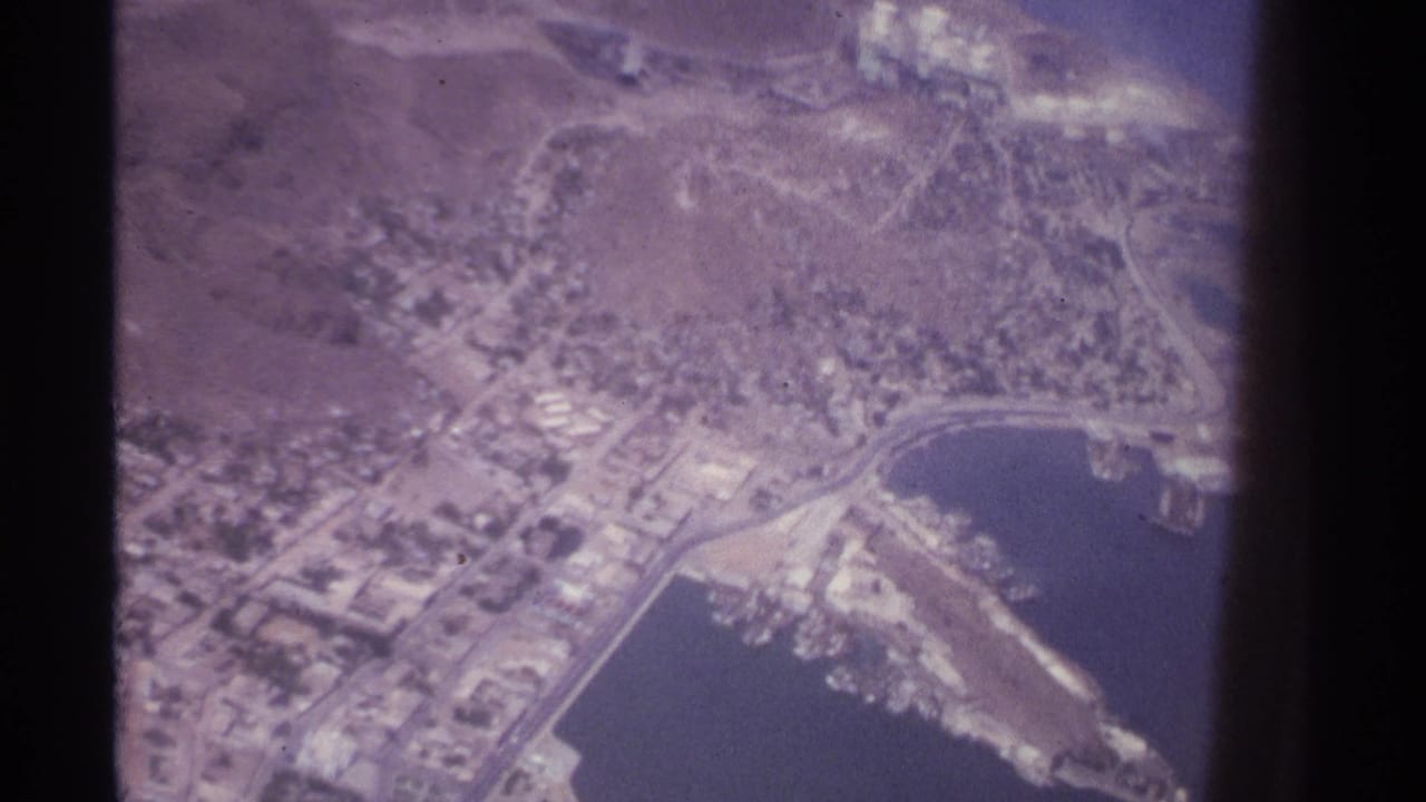 Aerial view of a coastal city beside a bay with roads, buildings, and a harbor area.
