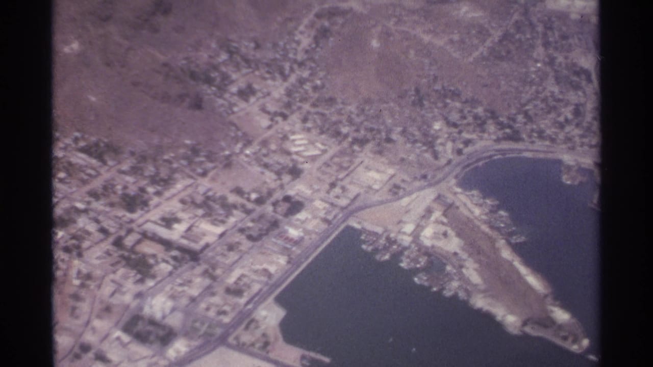 Aerial view of a bay, marina-like harbor, roads, and dense low-rise buildings.
