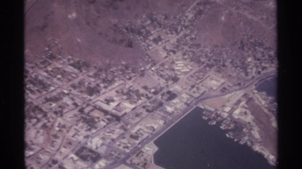 1974 La Paz aerial view showing a roadway network, pale rooftops, open land, and part of the coastal bay at frame edge.