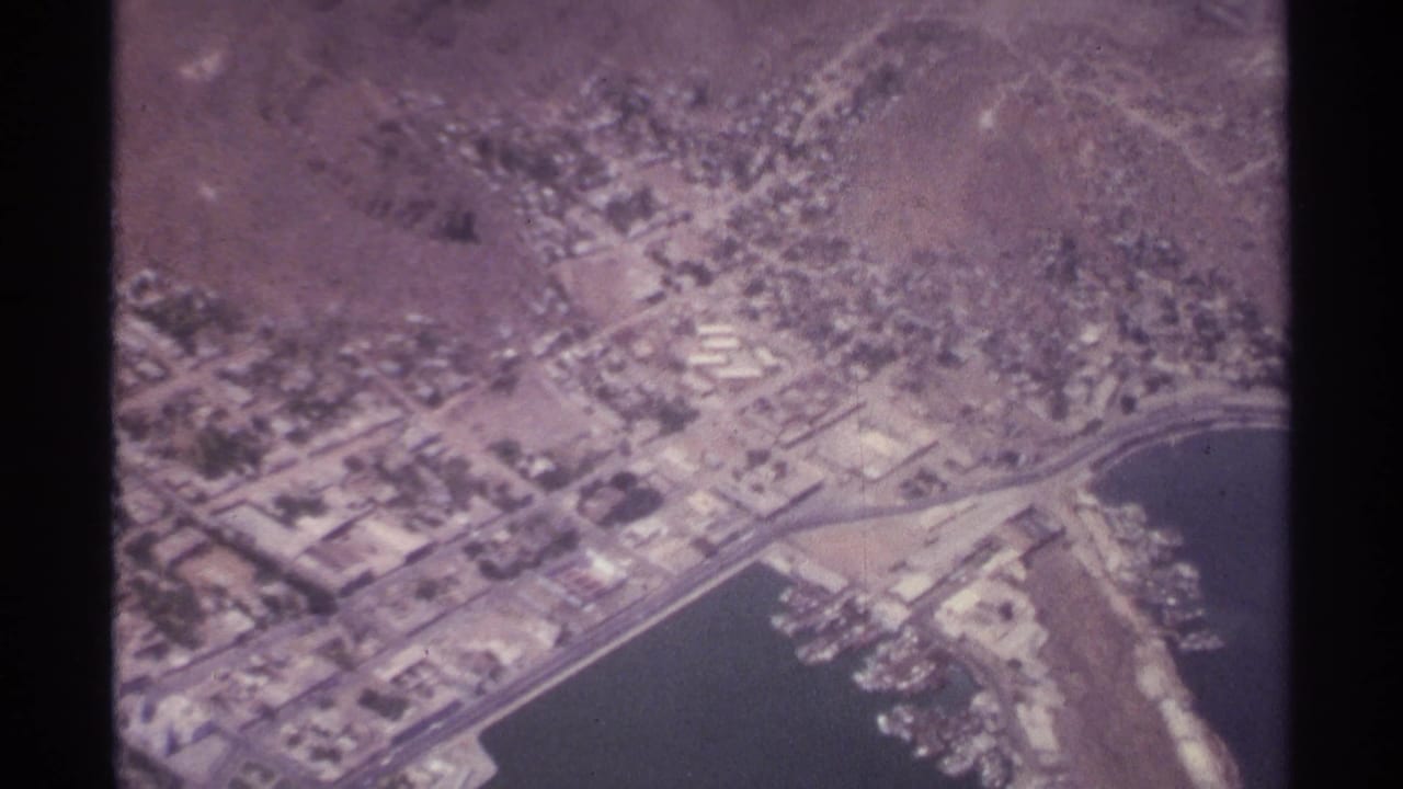 Aerial view of a coastal city, harbor edge, and dry hills from 8mm film.