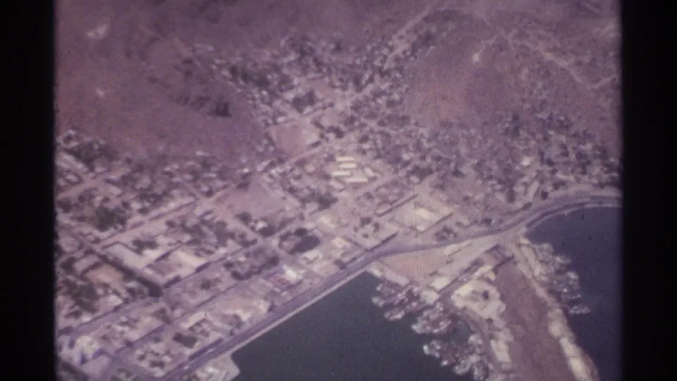 1974 aerial 8mm view over La Paz, Mexico, showing low-rise blocks near the harbor and arid hills beyond.