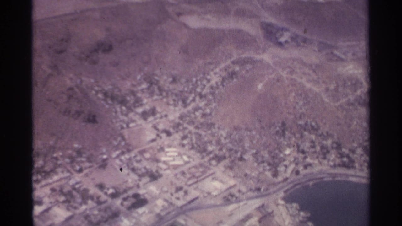 Aerial city and shoreline view with hills, roads, and harbor water visible.