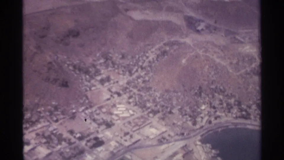 1974 aerial view over La Paz, Mexico, with roads and buildings along the shoreline and dry hills behind the city.