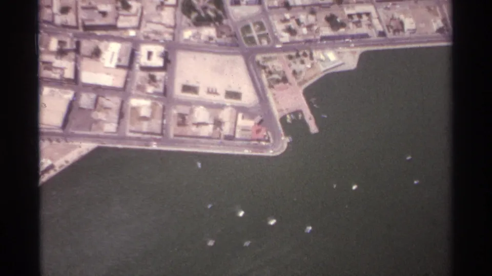 Closer 1974 aerial 8mm view of La Paz waterfront blocks, piers, harbor water, and several small boats offshore.