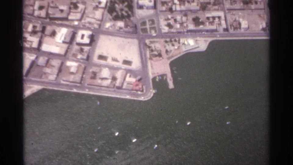 1974 La Paz, Mexico aerial frame showing low-rise waterfront blocks, streets, harbor water, and scattered small boats.