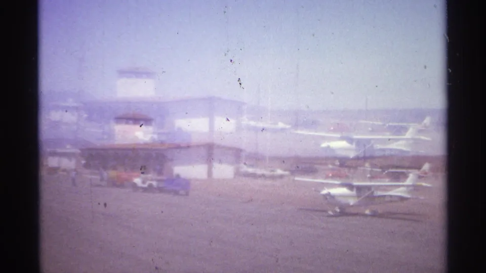 1974 La Paz, Mexico airfield view with several parked light aircraft, a control tower, tarmac, and hazy 8mm exposure.