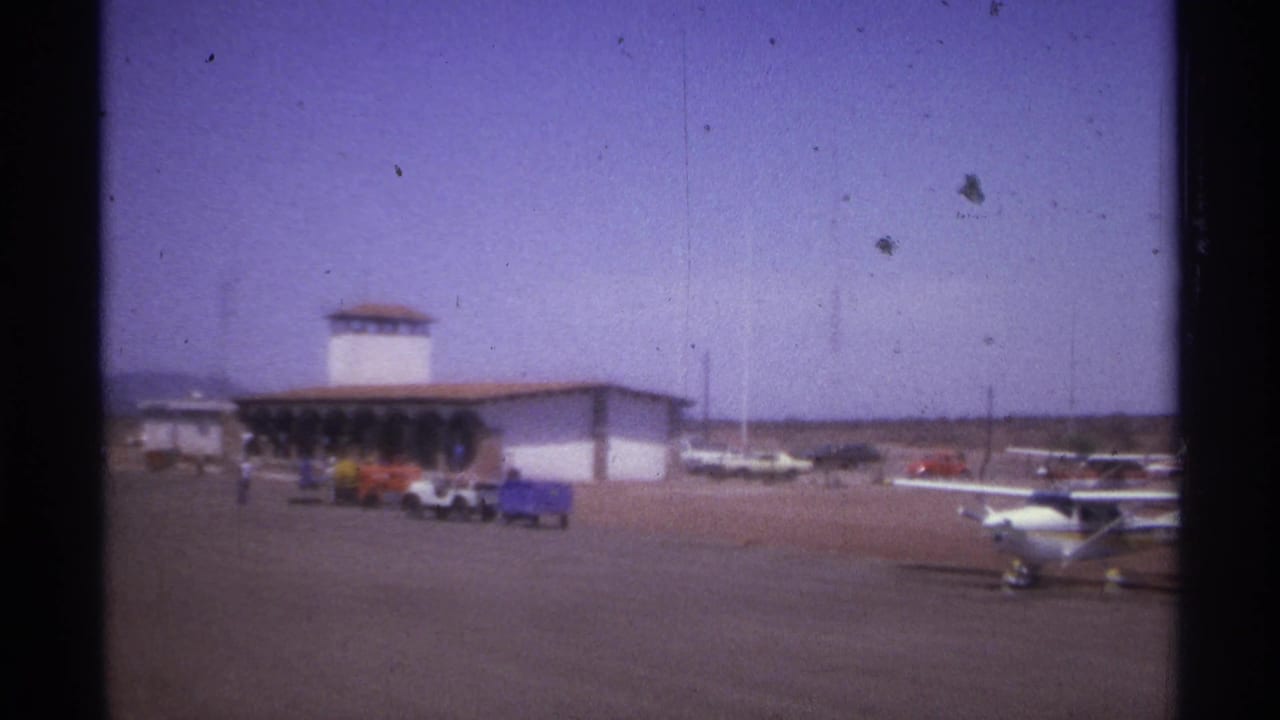 Small airport terminal and parked aircraft seen across an open tarmac.