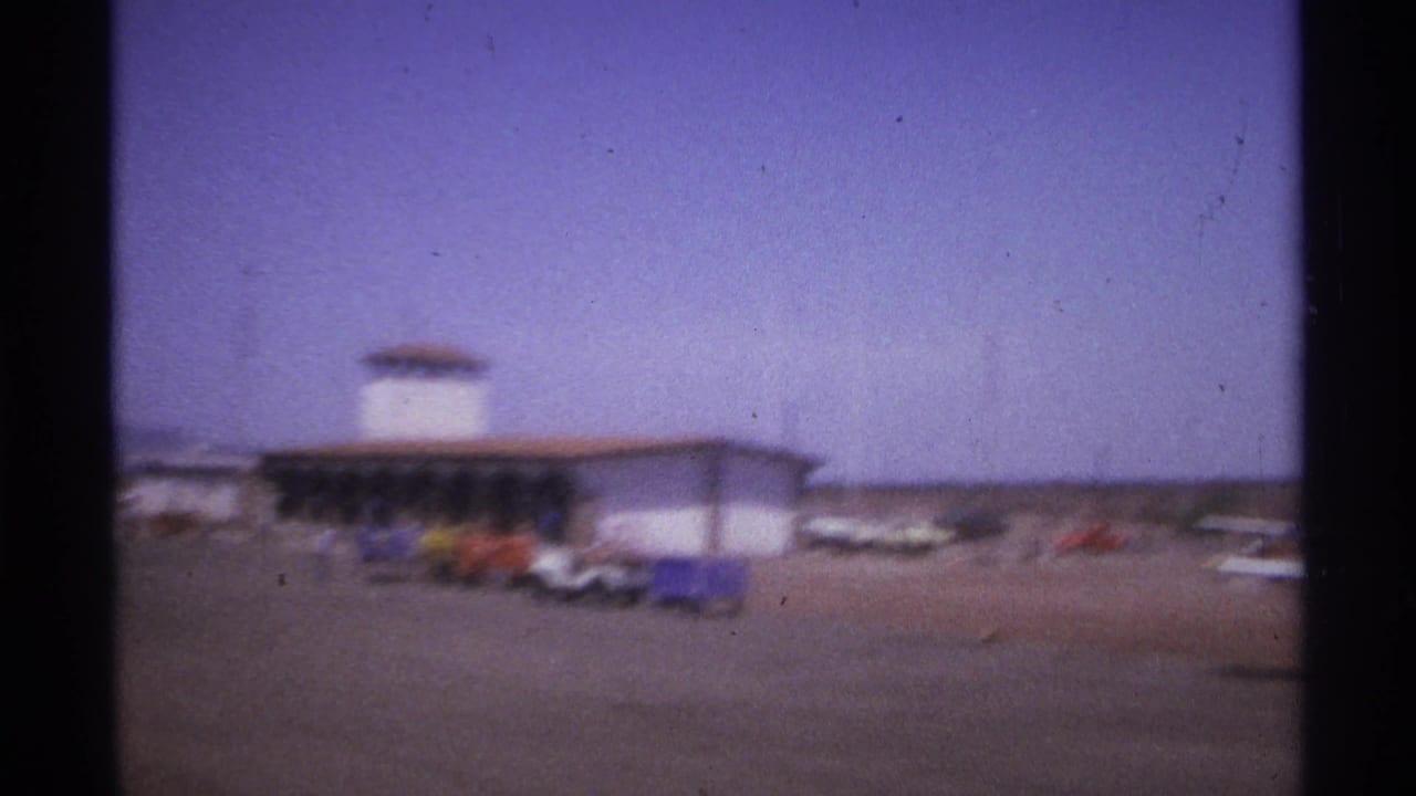 Airport building, parked planes, cars, and ground equipment on the tarmac.