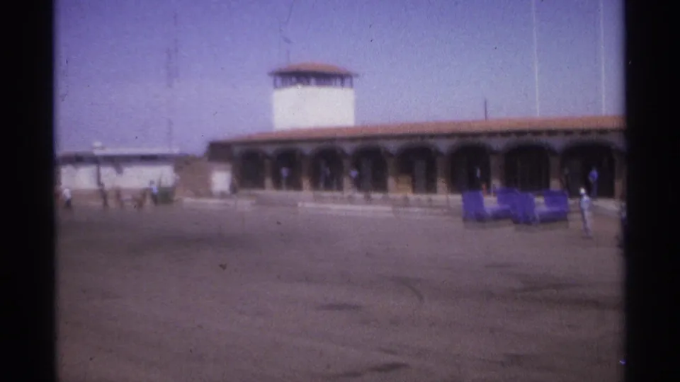 La Paz, Mexico airport terminal in 1974, showing arched openings, distant people, luggage carts, and a broad tarmac.