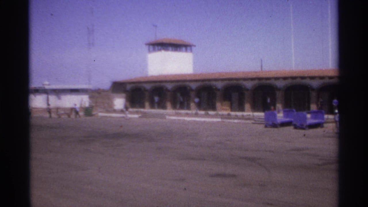 1974 La Paz, Mexico 8mm frame showing an arched building exterior with a white tower, carts, and distant pedestrians.