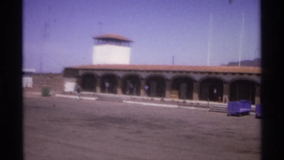 1974 La Paz, Mexico 8mm frame with the arched facade closer in view, blue carts, steps, and tower.