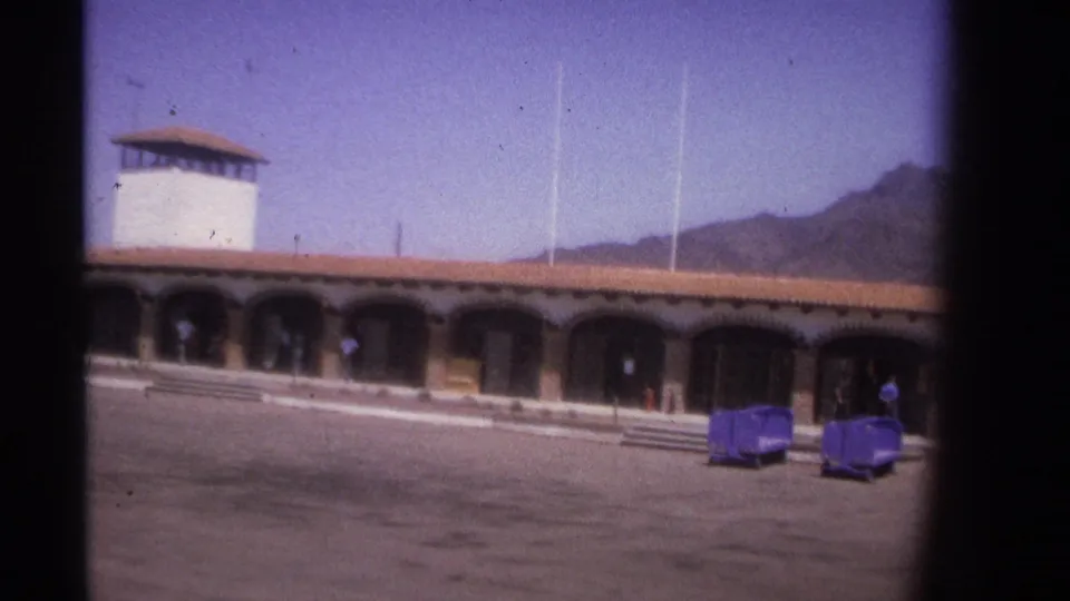 1974 La Paz, Mexico frame showing the arched building, luggage carts, pedestrians, and distant hills.
