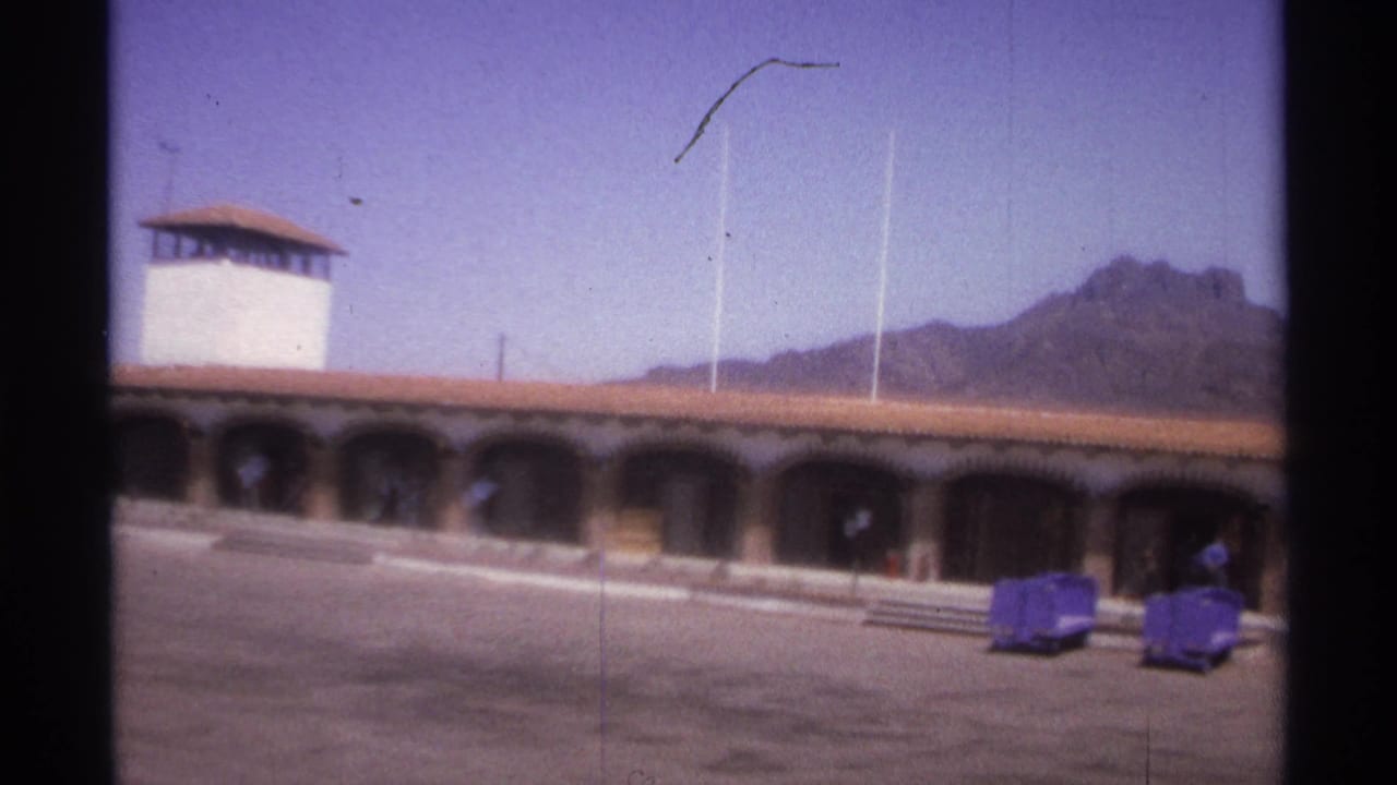 Arched building and tower beside an open plaza with mountains behind.