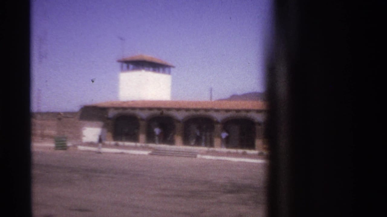 White tower and arched building across a mostly empty paved plaza.