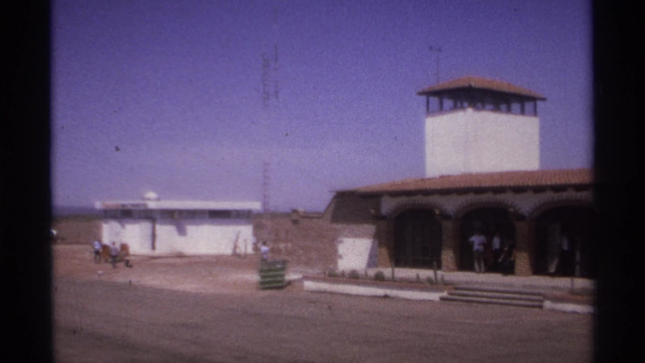 White tower and arched entrance beside an open paved area with several people nearby.