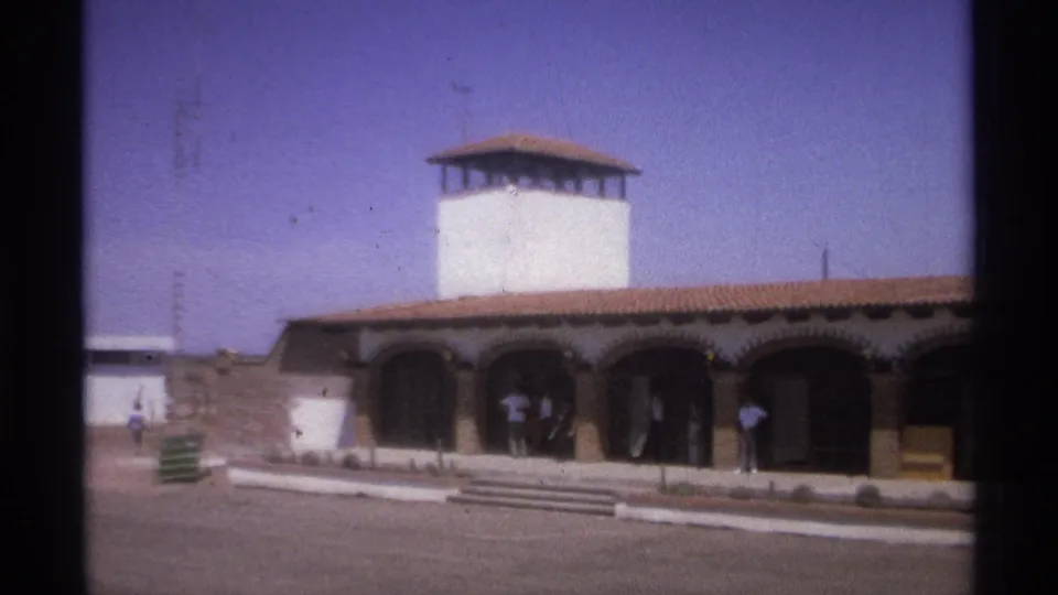 1974 La Paz, Mexico frame showing the towered arched building in a desert setting, with people standing near shaded entry bays.