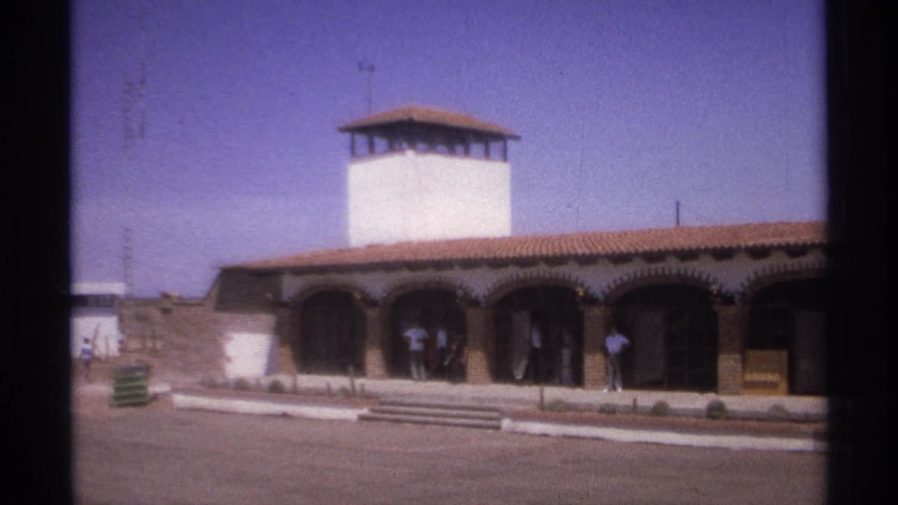 White tower above a terracotta-roofed building with arched entryways and people near the entrance.