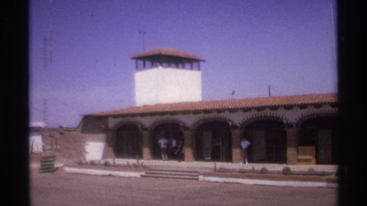 White arched building with tower under a clear sky and people near the entrance.