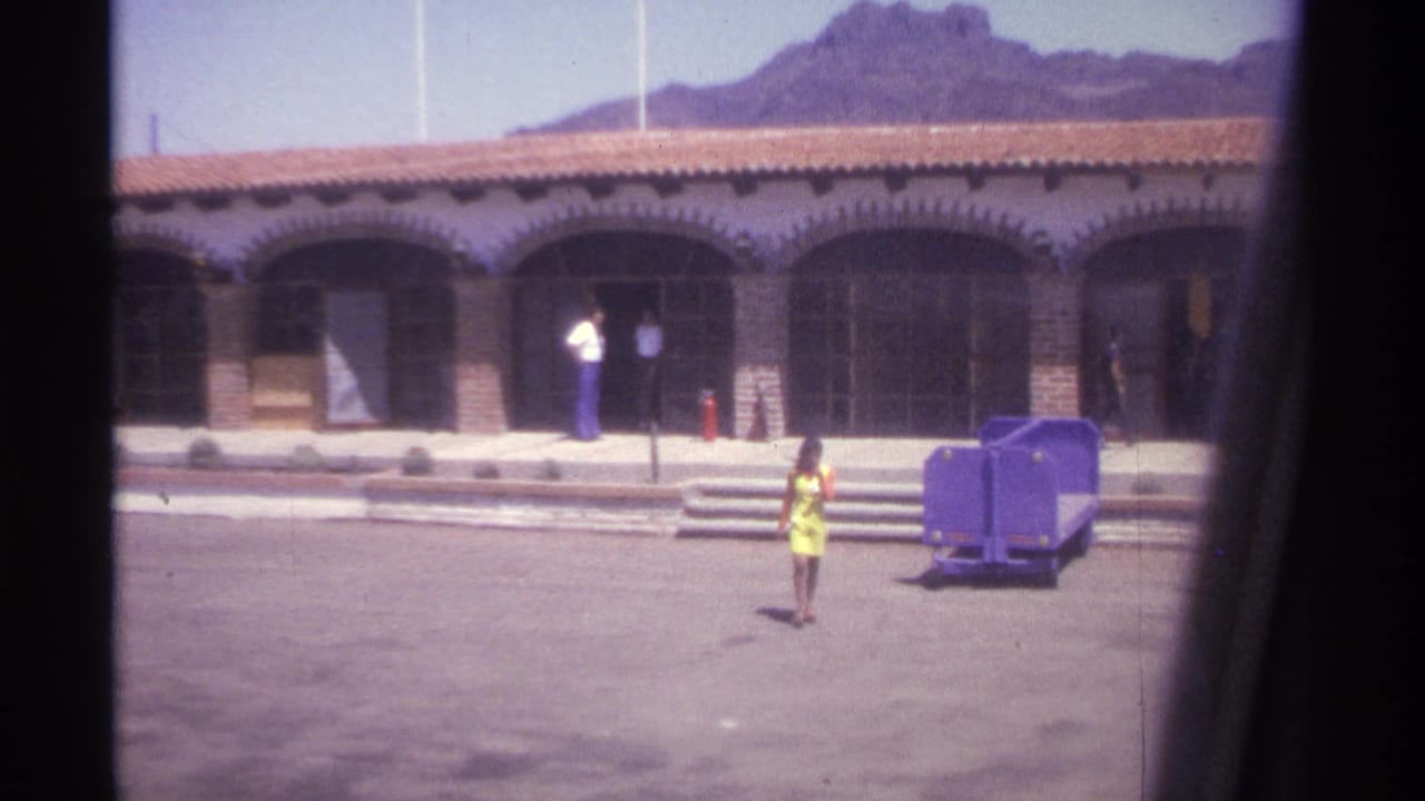 Woman in a yellow dress walks across a paved area near a purple utility cart.