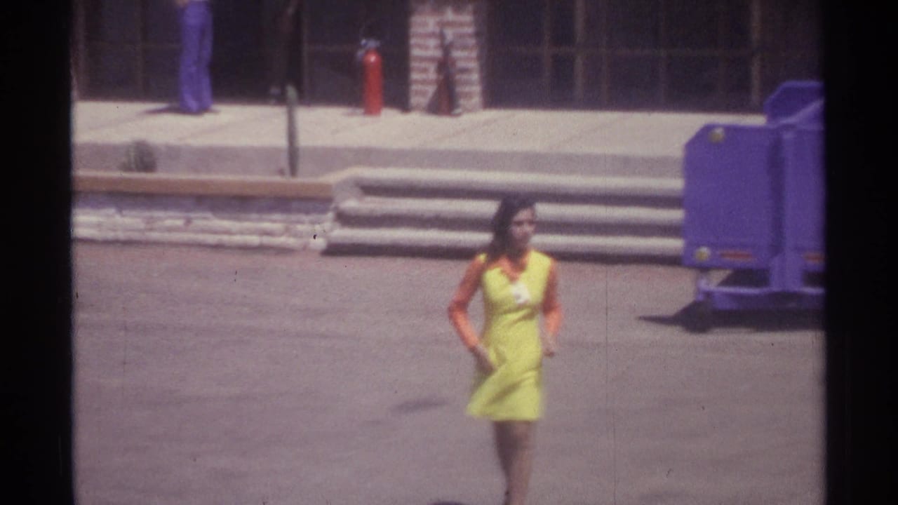 In La Paz, Mexico in 1974, a young woman in a bright uniform walks toward the camera across an open paved lot.