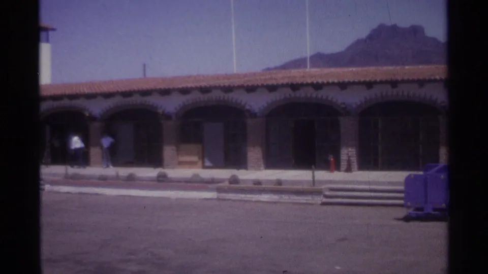 Wide 1974 La Paz view of an arched building and open paved area, with a purple cart and mountain visible beyond.