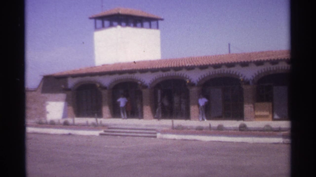 Building exterior with arched doorways, front steps, and people standing in shade near the entrance.