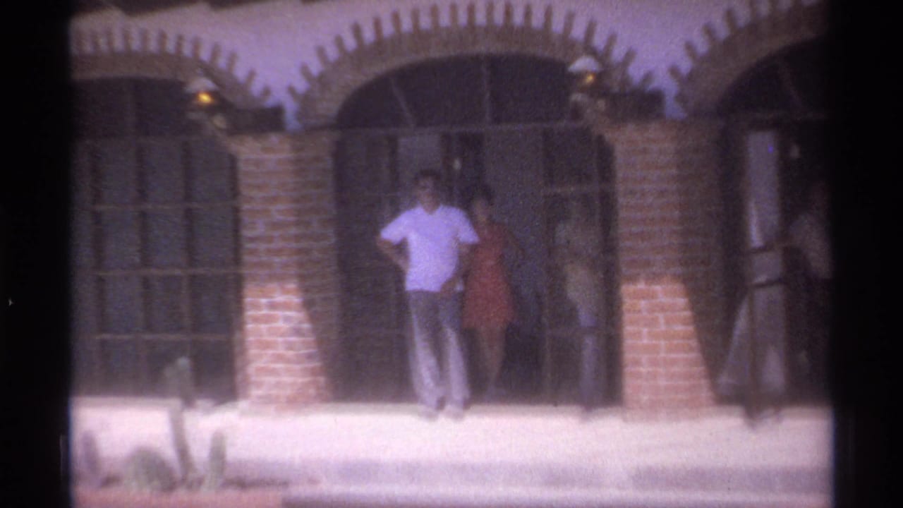 A man and woman stand in a doorway while others remain nearby.
