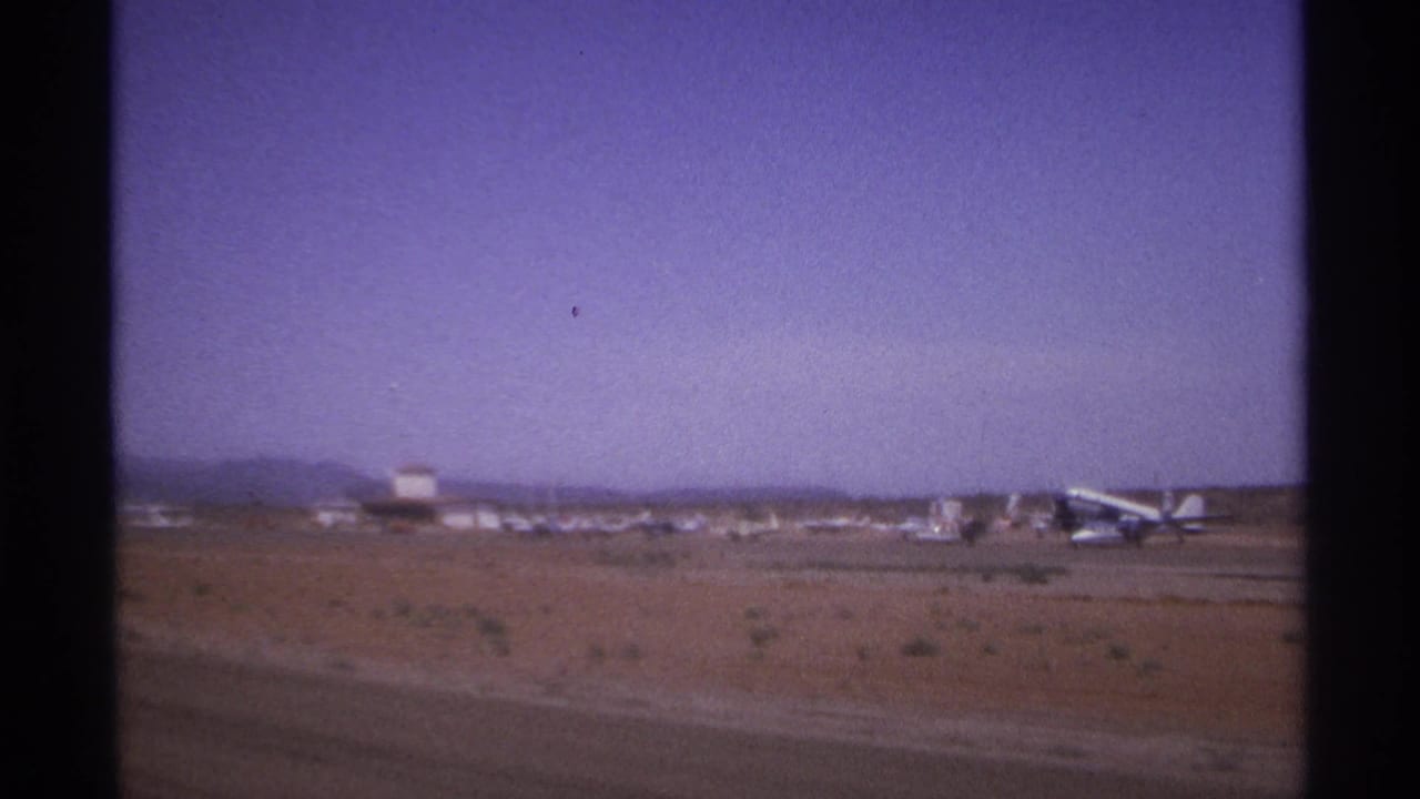 Desert airfield with small aircraft under a hazy purple sky.