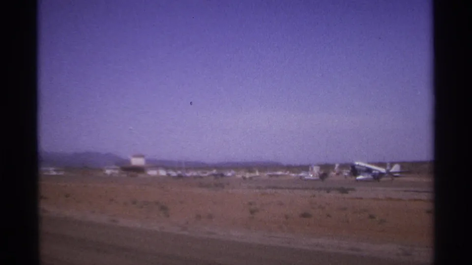 A desert airfield in the supplied La Paz setting shows small aircraft and low equipment beneath a hazy sky.
