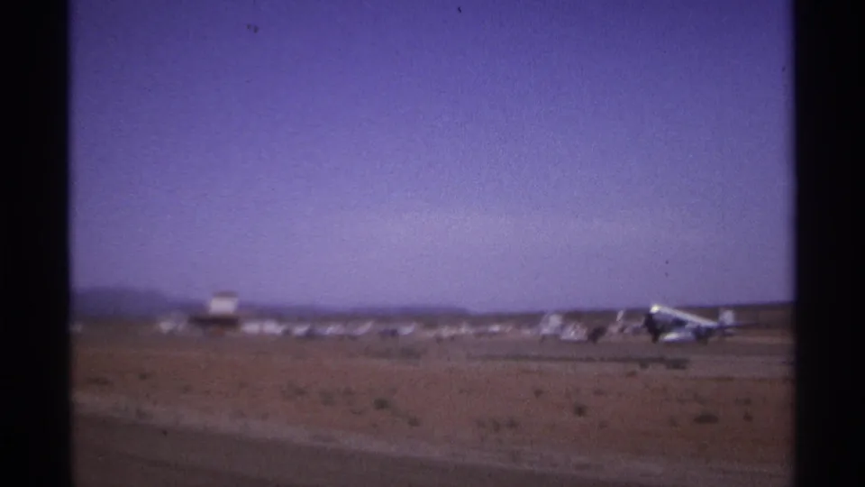 A wide 8mm view shows a small aircraft near a runway with distant structures and hills in La Paz, Mexico.