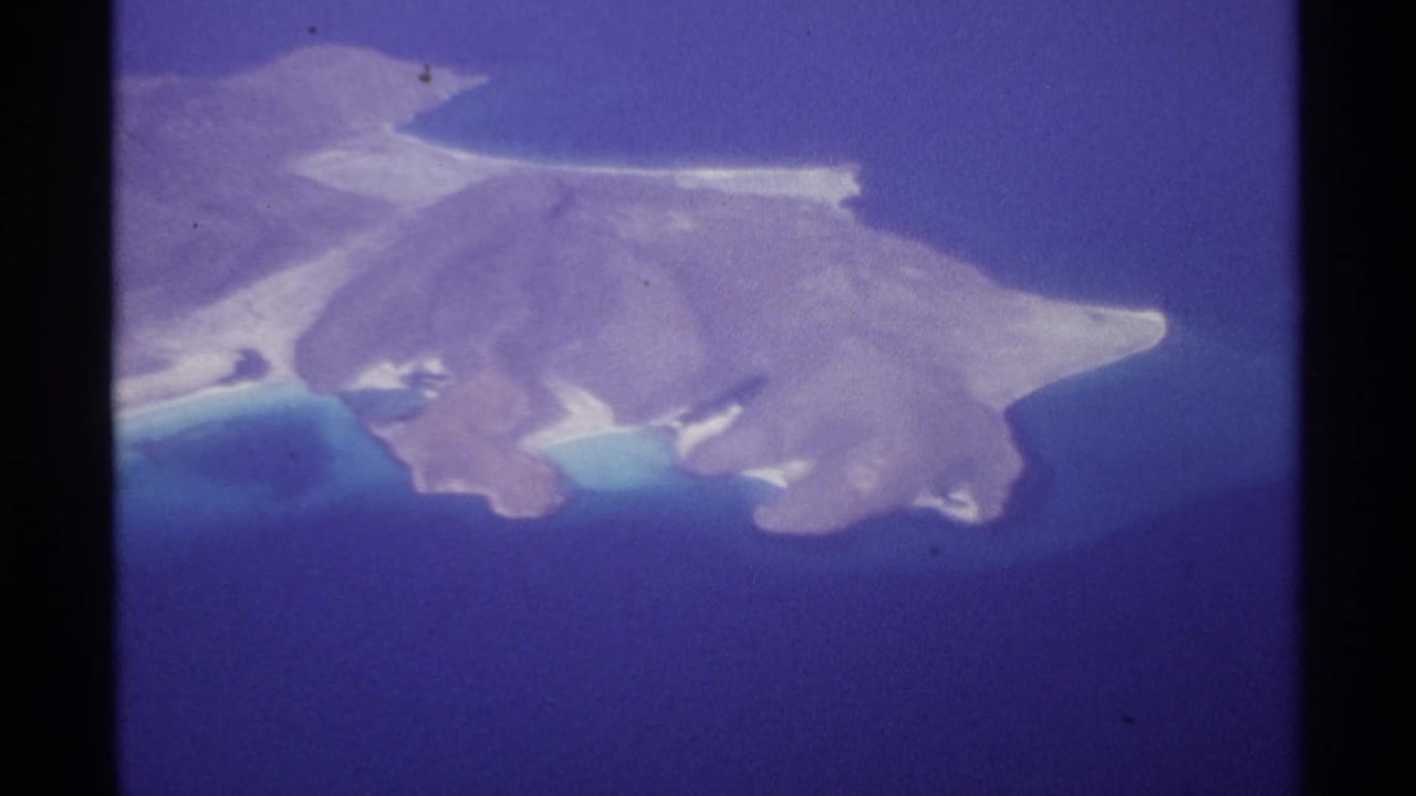 Aerial view of a brown island surrounded by deep blue water and pale beaches.