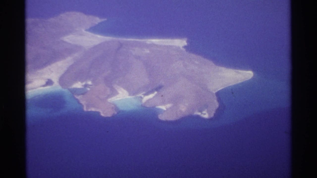 Brown island with narrow white beaches seen from above in blue ocean water.