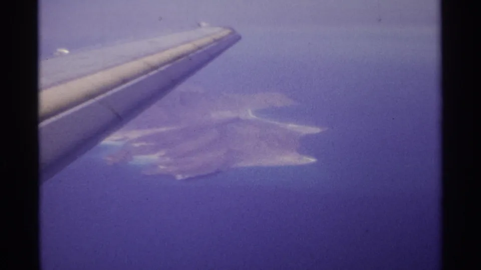Vintage 8mm aerial frame from La Paz, Mexico, with the aircraft wing foregrounding an island coastline.