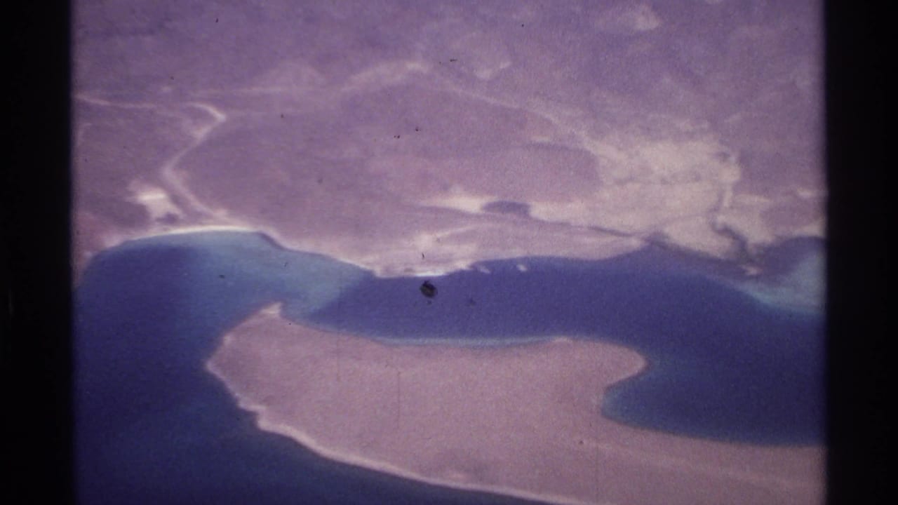 Aerial view of sandy island, turquoise water, and arid coastline.