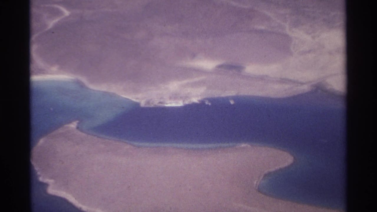 Aerial view of sandy coastline beside deep blue water with a pale shoreline structure.
